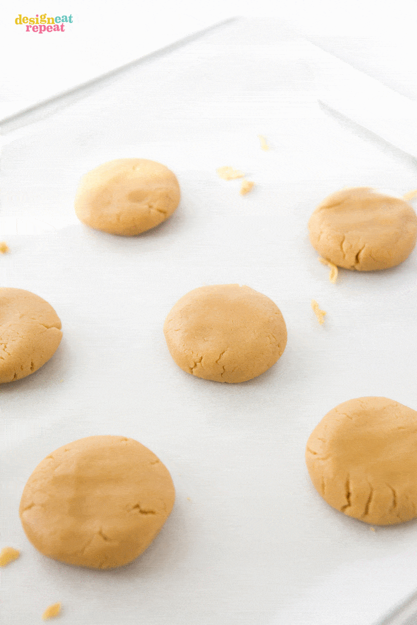 Peanut butter cookie dough balls being shaped and flattened on baking sheet.