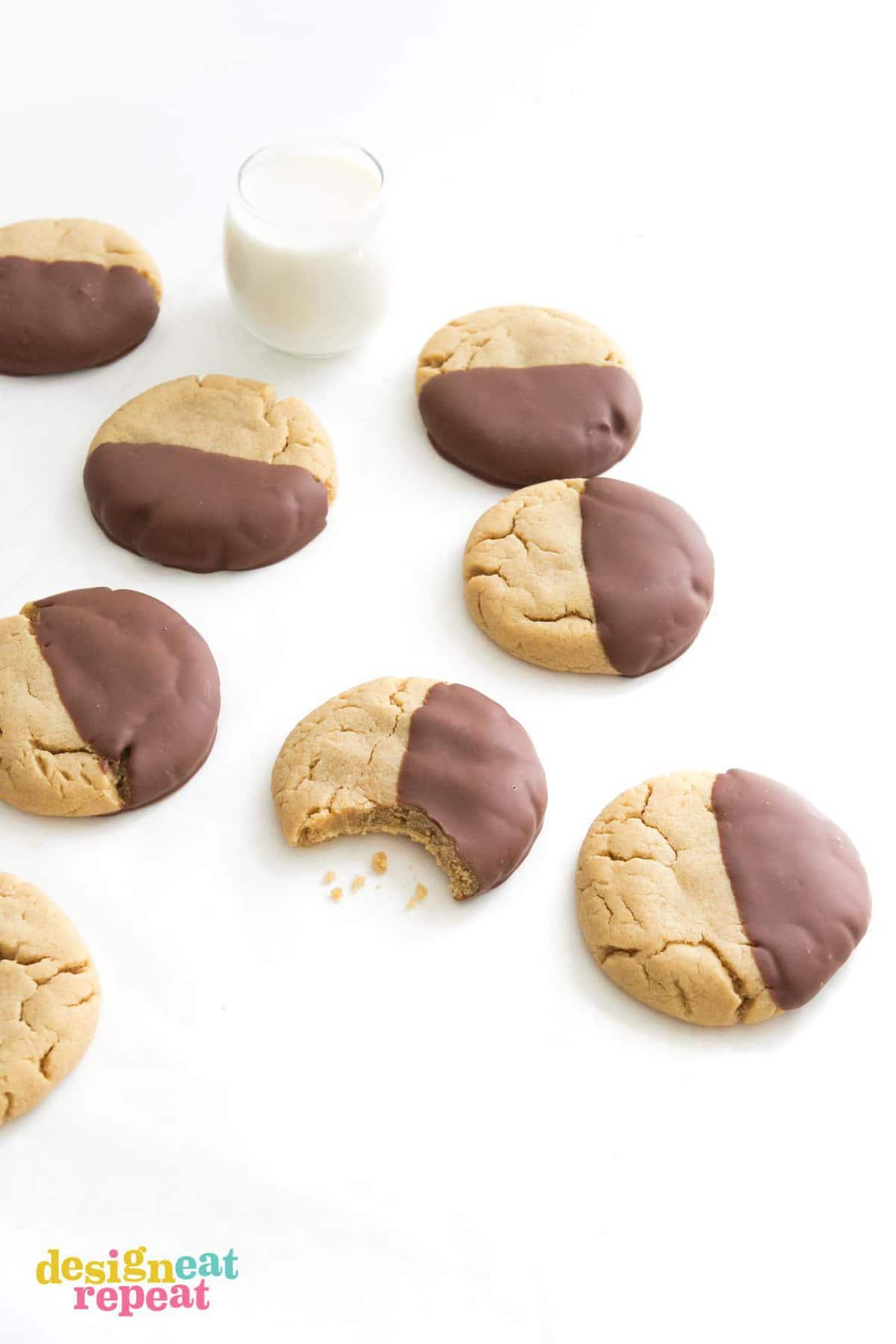 Table of peanut butter cookies dipped in chocolate with bite and glass of milk.