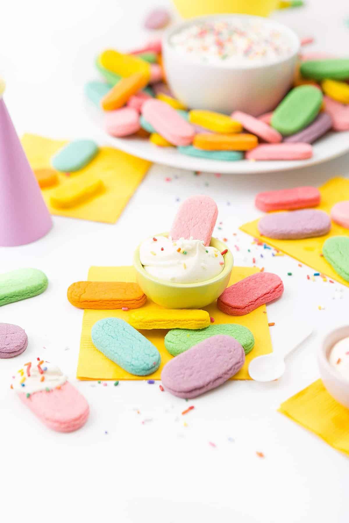 Pink sugar cookie being dipped in small bowl of frosting.