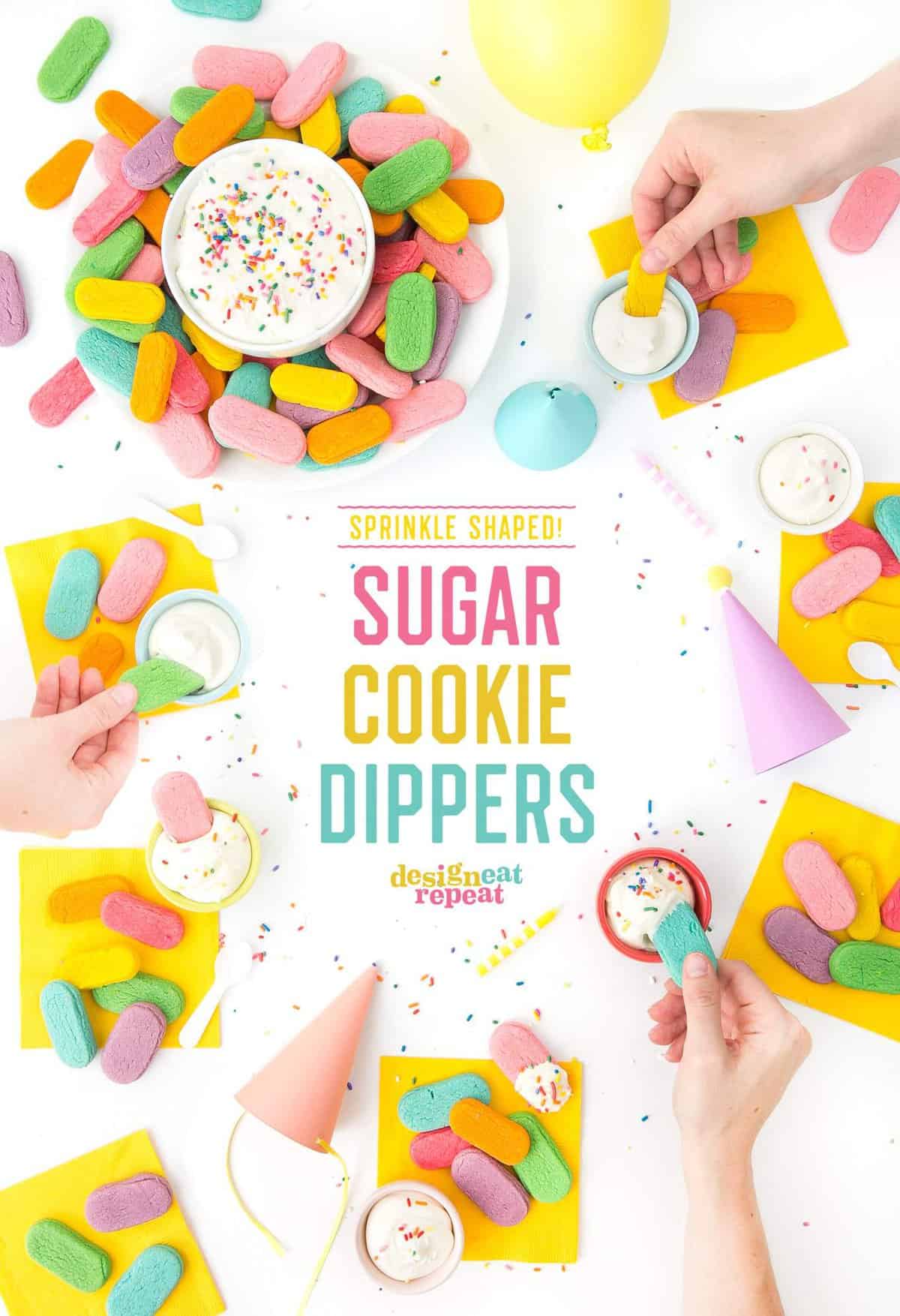 Overhead table shot of plates of sugar cookies shaped like sprinkles! Hands dipping cookies into bowls of icing, aside of party hats and yellow napkins.