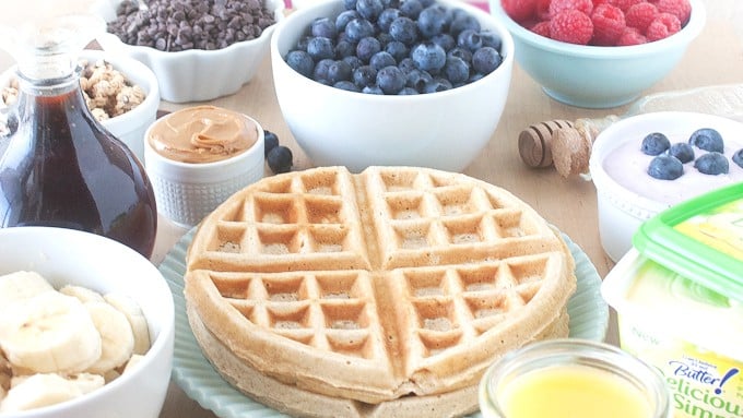 Plate of whole wheat waffles, bowl of blueberries, raspberries, bananas, peanut butter, and chocolate chips.