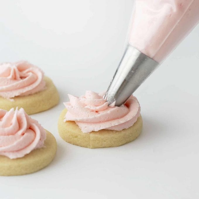 piping pink buttercream frosting on sugar cookies 