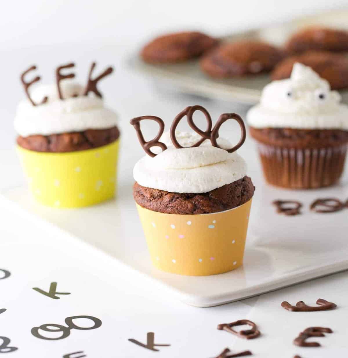 Chocolate cupcake with vanilla frosting in orange cupcake wrapper. With chocolate BOO word on top for edible Halloween cupcake topper.