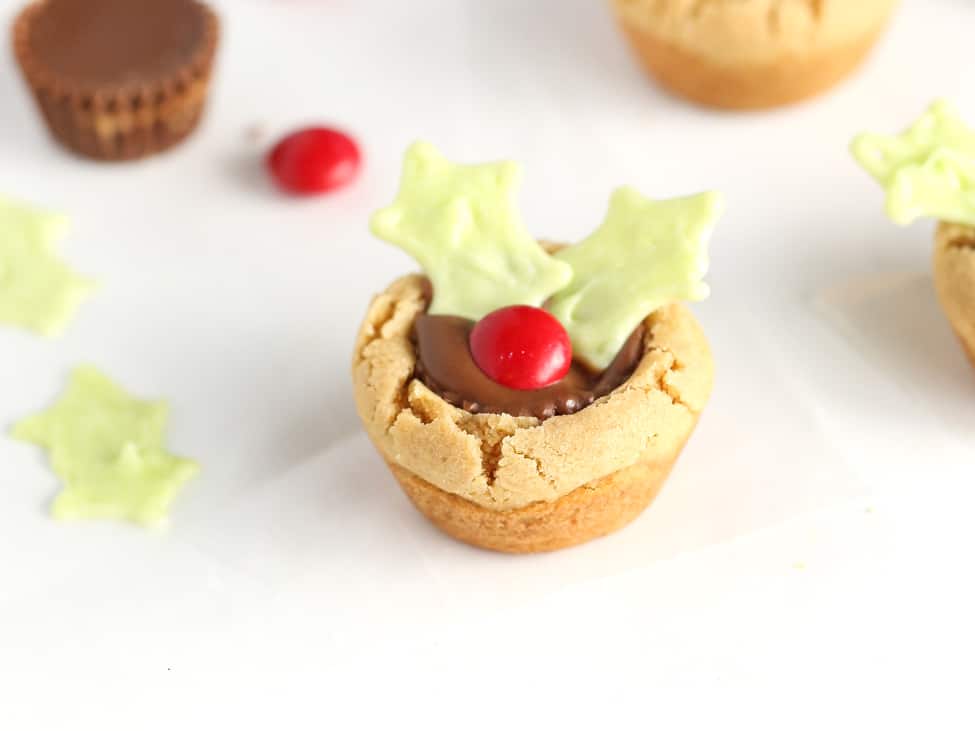 Reeses peanut butter cup cookie decorated like holly leaf to make easy Christmas holly cookie cups.