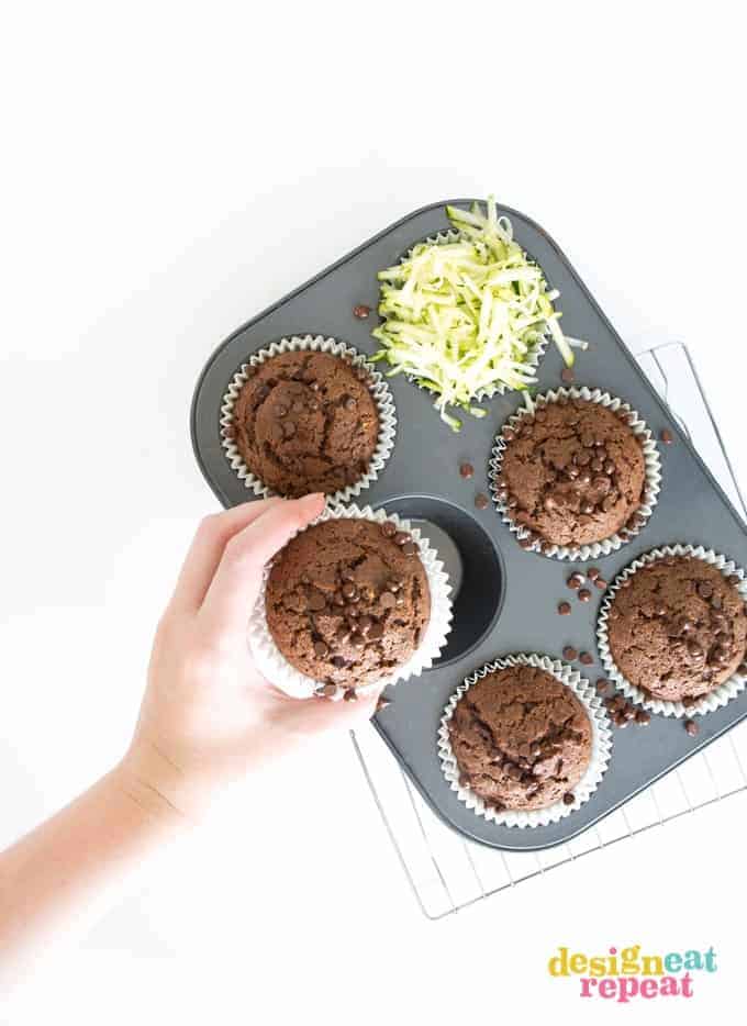 Hand reaching out and picking up chocolate muffin from cupcake pan.