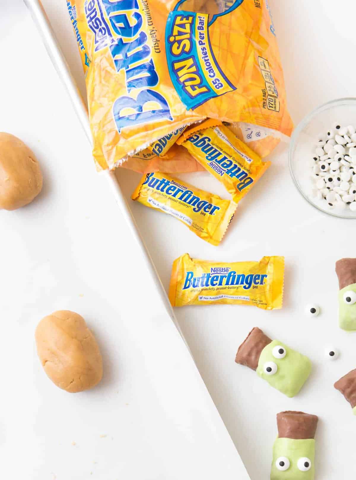 Open bag of Butterfinger fun size candy bars with balls of peanut butter cookie dough on cookie sheet ready to be baked. 