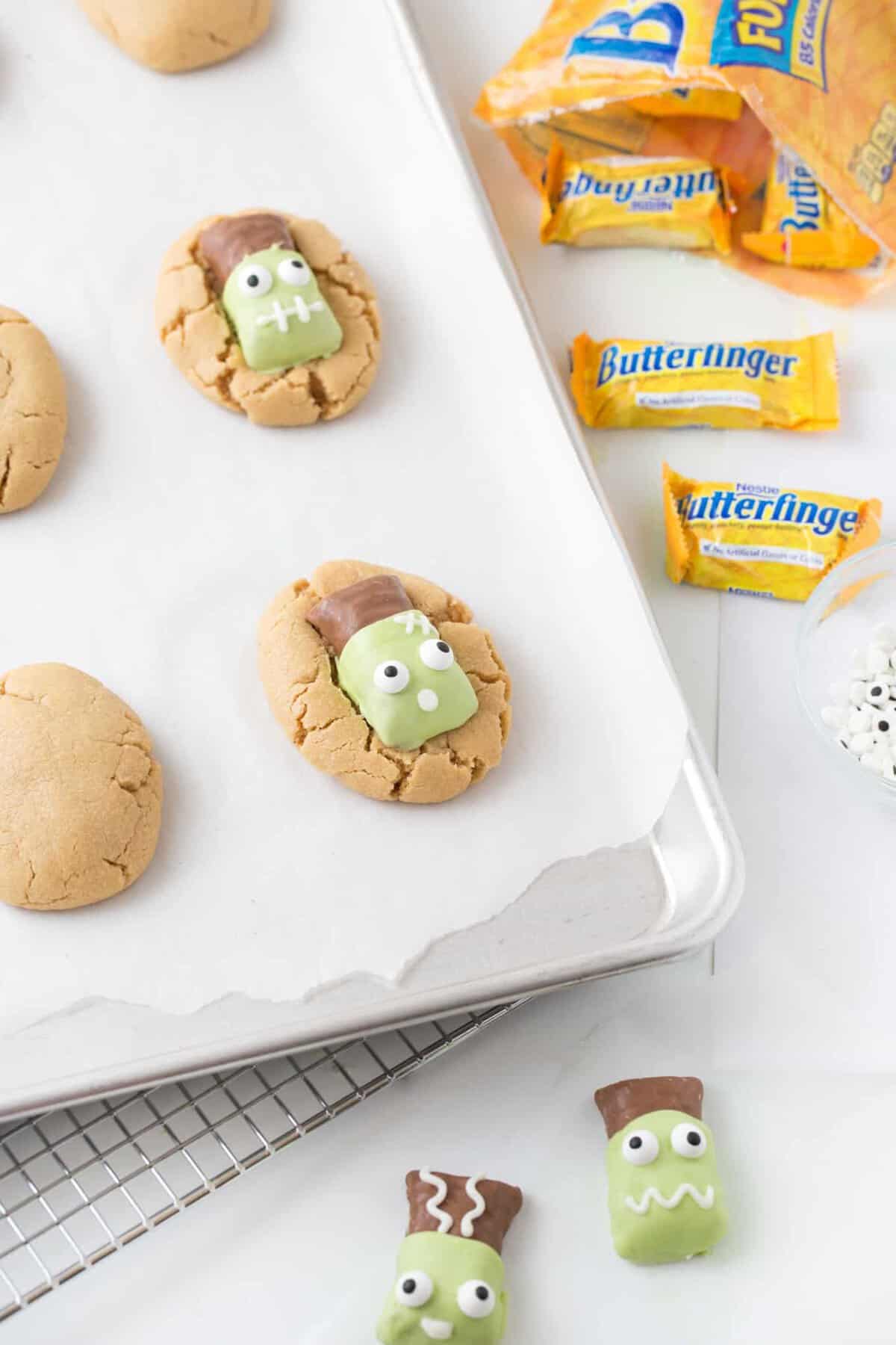 Peanut butter cookies on baking tray topped with decorated Frankenstein Butterfinger candy bars.