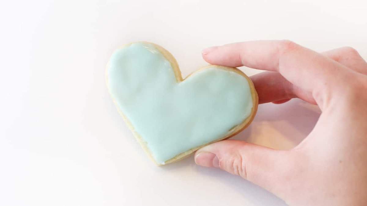 Hand holding blue heart sugar cookie.