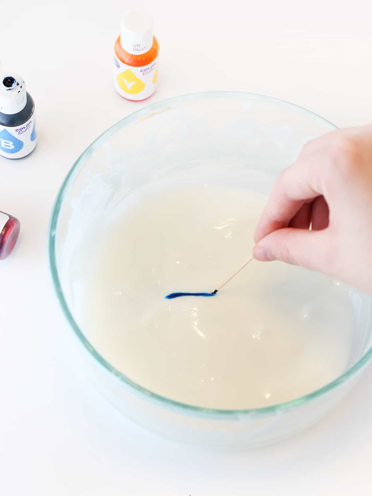 Hand holding toothpick that is adding blue food coloring to white cookie icing.