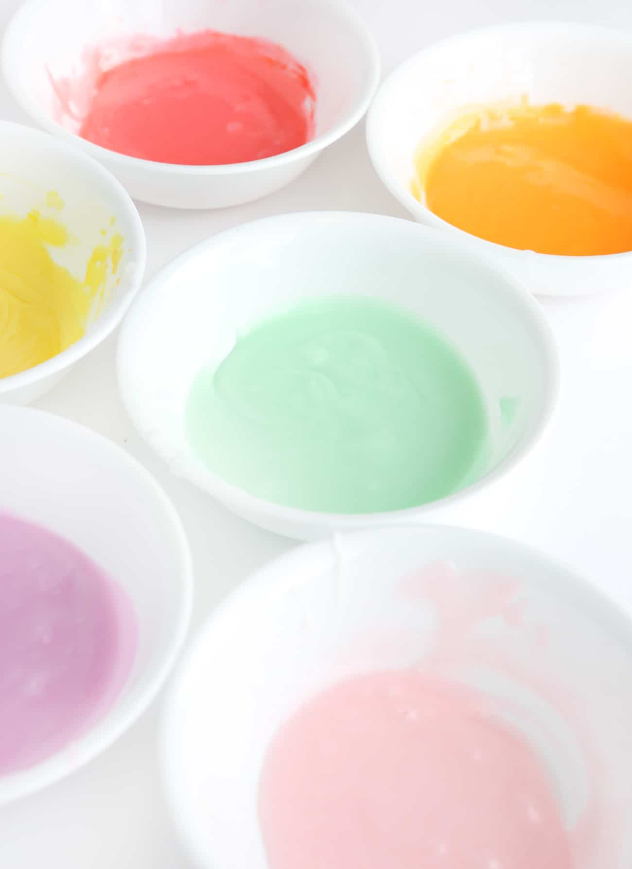 White bowls with different colors of rainbow cookie icing.