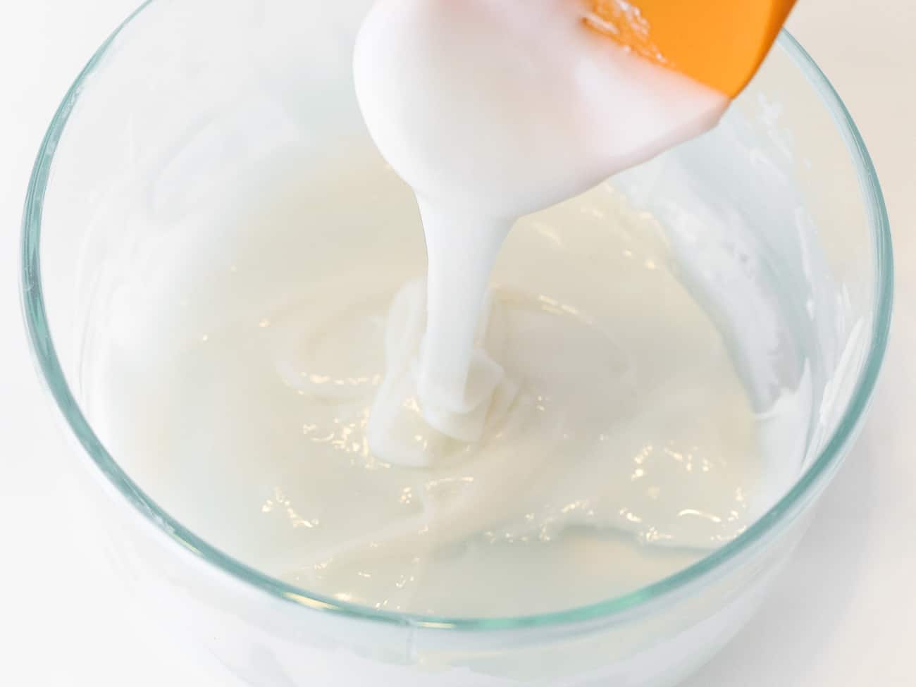 A orange spatula and bowl of whitee cookie icing.