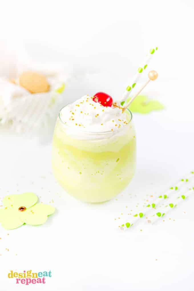 Mint Shamrock milkshake in glass cup topped with whipped cream, a cherry, and gold sprinkles.