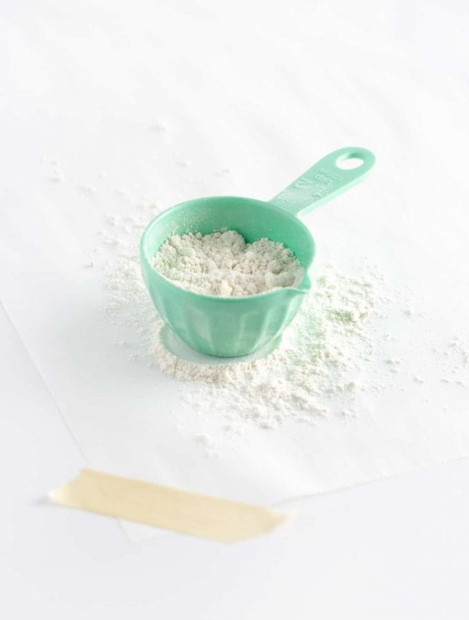 Blue measuring cup of flour on parchment paper