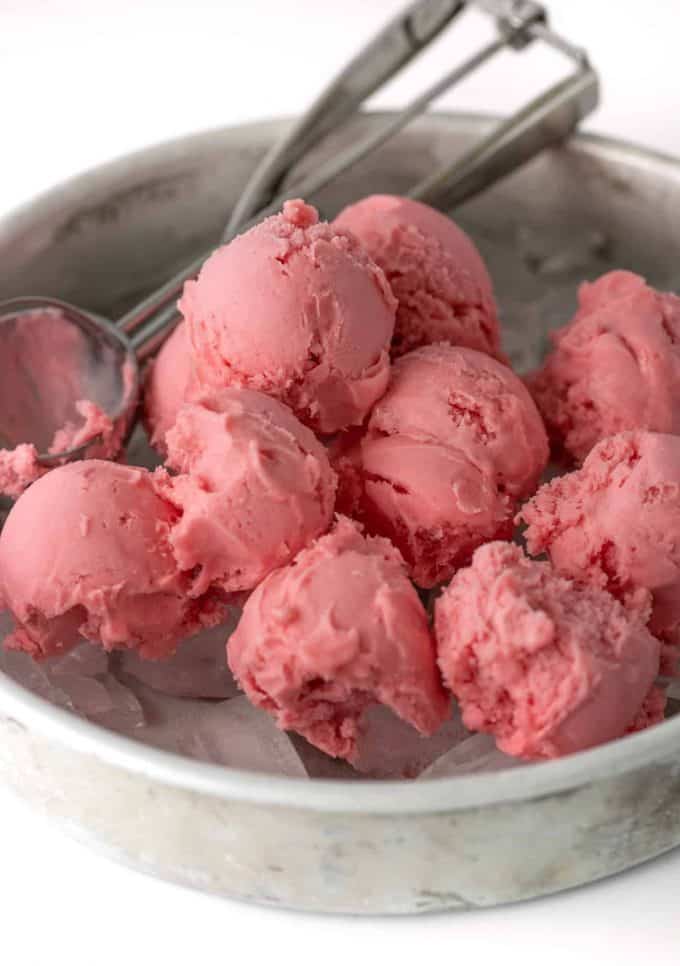 Scoops of raspberry sherbet on ice in metal baking pan