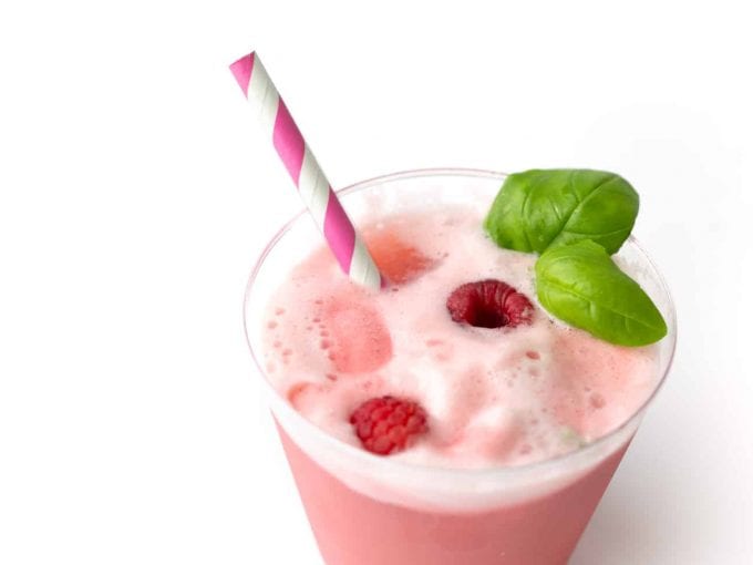 Cup of Raspberry Sherbet Punch with fresh raspberries, pink straw, and basil leaves