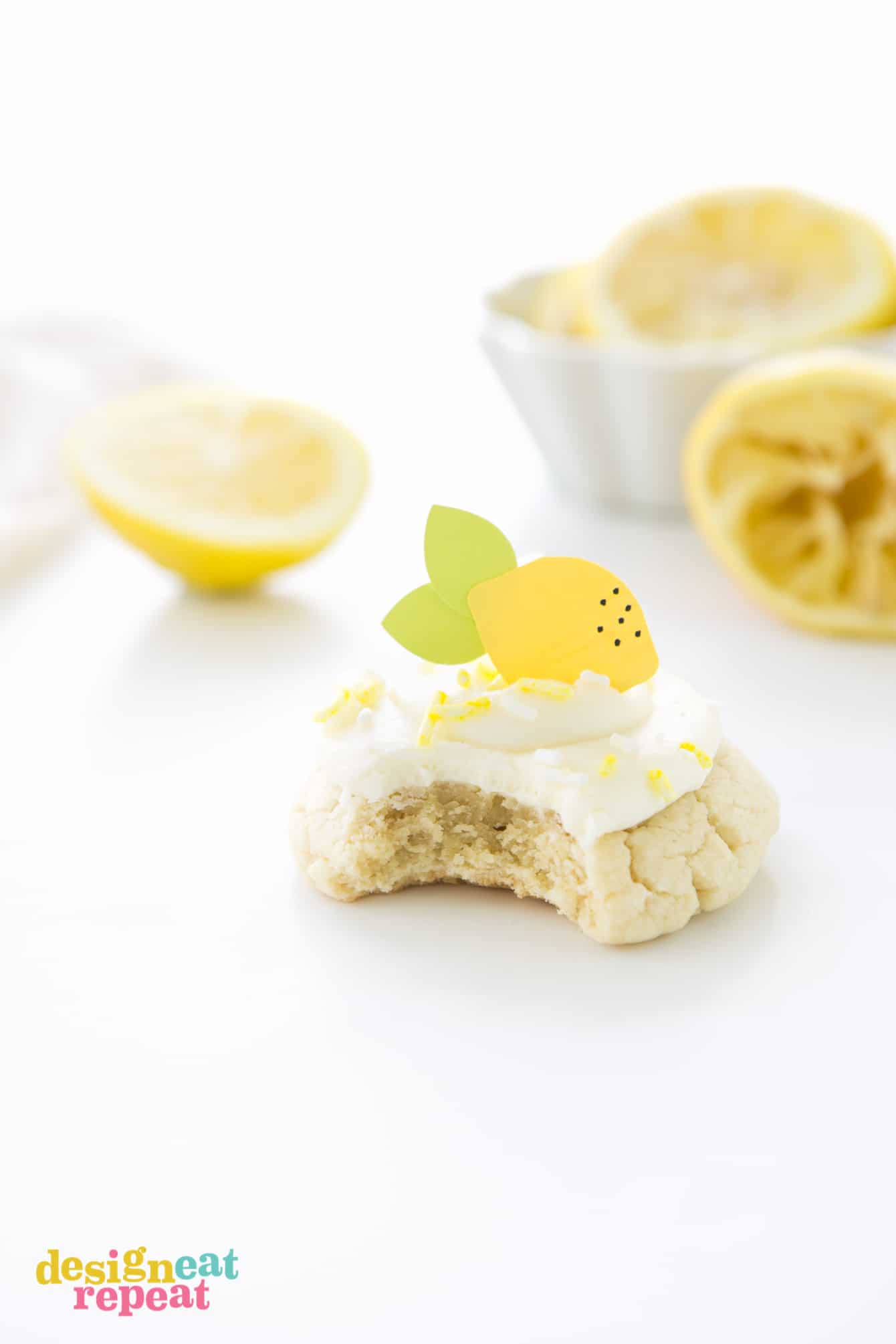 Lemon sugar cookie with bite taken out of it. Topped with frosting, sprinkles, and paper lemon topper.