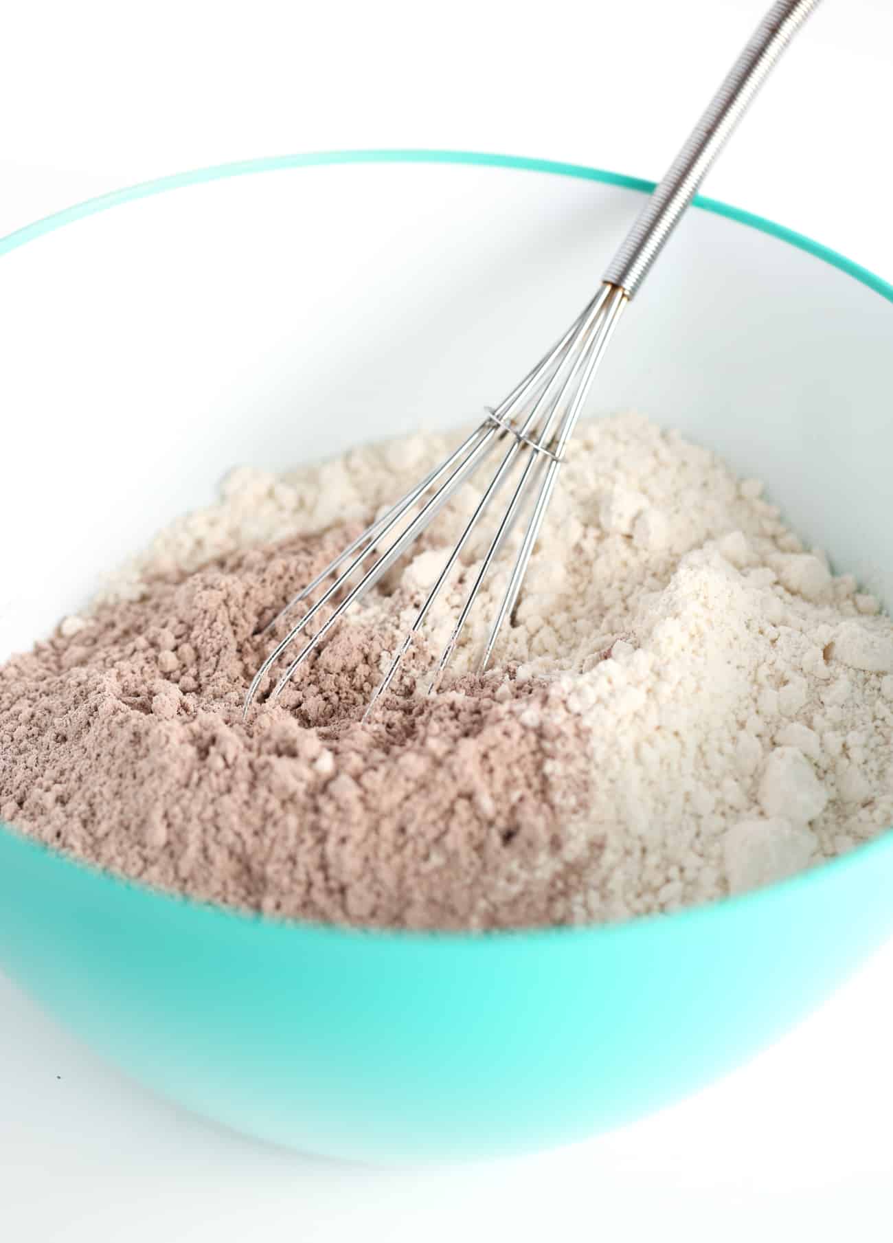 Metal whisk stirring blue bowl of brownie mix and flour for chocolate brownie cookies.