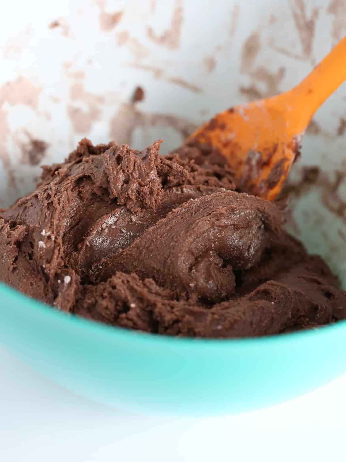 Orange sillicon spatula stirring thick chocolate cookie dough for chocolate brownie cookies.