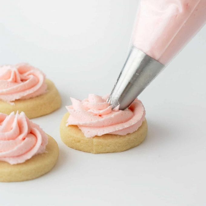 Sugar cookie being piped with swirl pink buttercream frosting