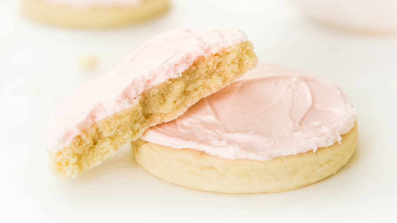 Stack of two large sugar cookies with pink frosting with bite taken out of one.